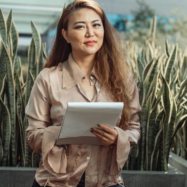 Confident Asian woman holding a notebook, sitting outdoors in a relaxed business setting.